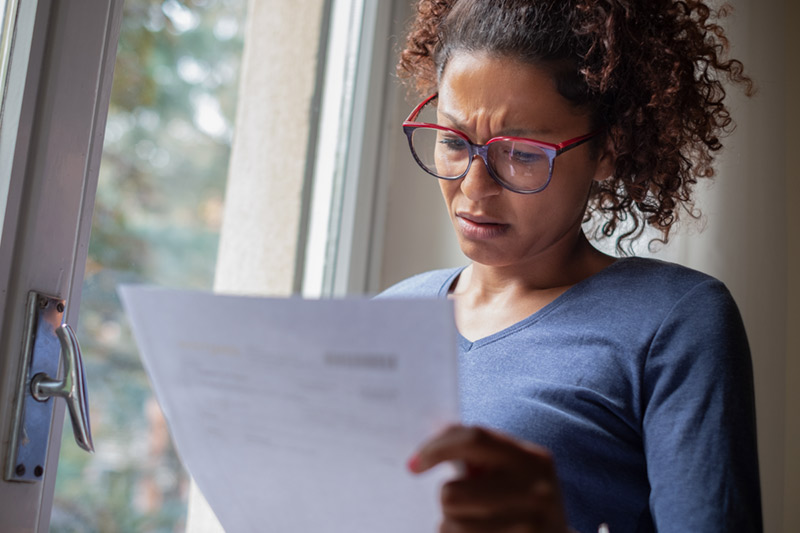 A woman looking concerned while reading a bill.