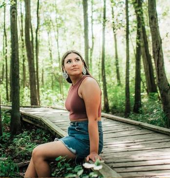 A female sitting at the edge of  the boardwalk path in Sifton Bog looking up to the trees surrounding her located