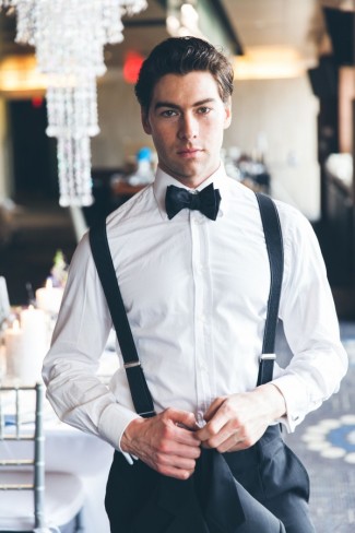 Groom wearing tux with black bow tie and black suspenders 