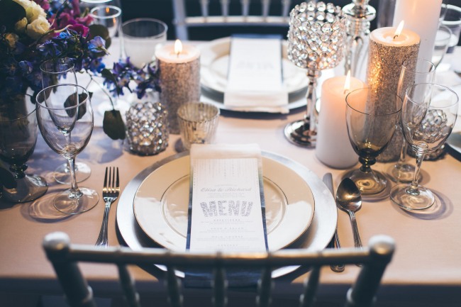 White Wedding reception menu with hints of silver. Puple flower centerpeice with silver sparkle glitter candle sticks, crystal jewel candle holders silver 