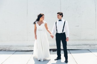 Bride wearing a durga-kali dress and groom wearing black tux with bow tie holding hands on roof 