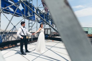 Bride wearing a durga-kali dress and groom wearing black tux with bow tie holding hands on roof top 