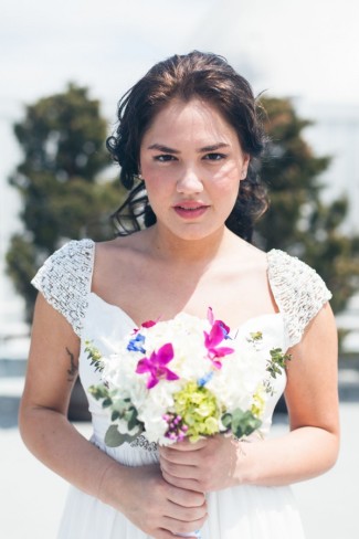 Bride wearing a durga-kali bridal dress with beaded sleeves holding a bouquet of white pink and green flowers 