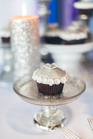 Silver glitter candle in back ground. Cup cake decorated with small white flowers on small glass cake stand 