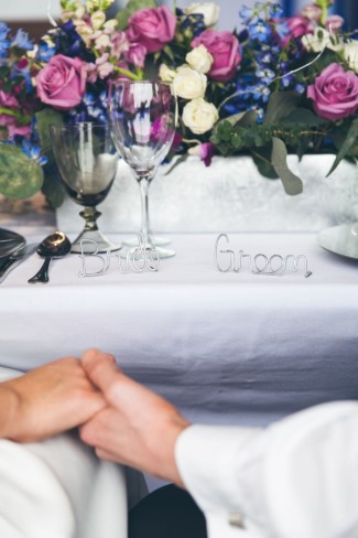 purple, blue, white, mauve and green floral bouquet centerpiece with metal bride and groom in cursive writing