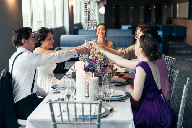 Bride and groom with bridal party have a toast at a purple and silver theme table