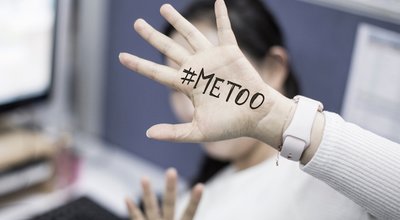 Close up portrait of unknown young woman covering her face w/ #Metoo hashtag word on palm of hand, taken in the office. Me too movement. Anti sexism protest against inappropriate behavior towards wome