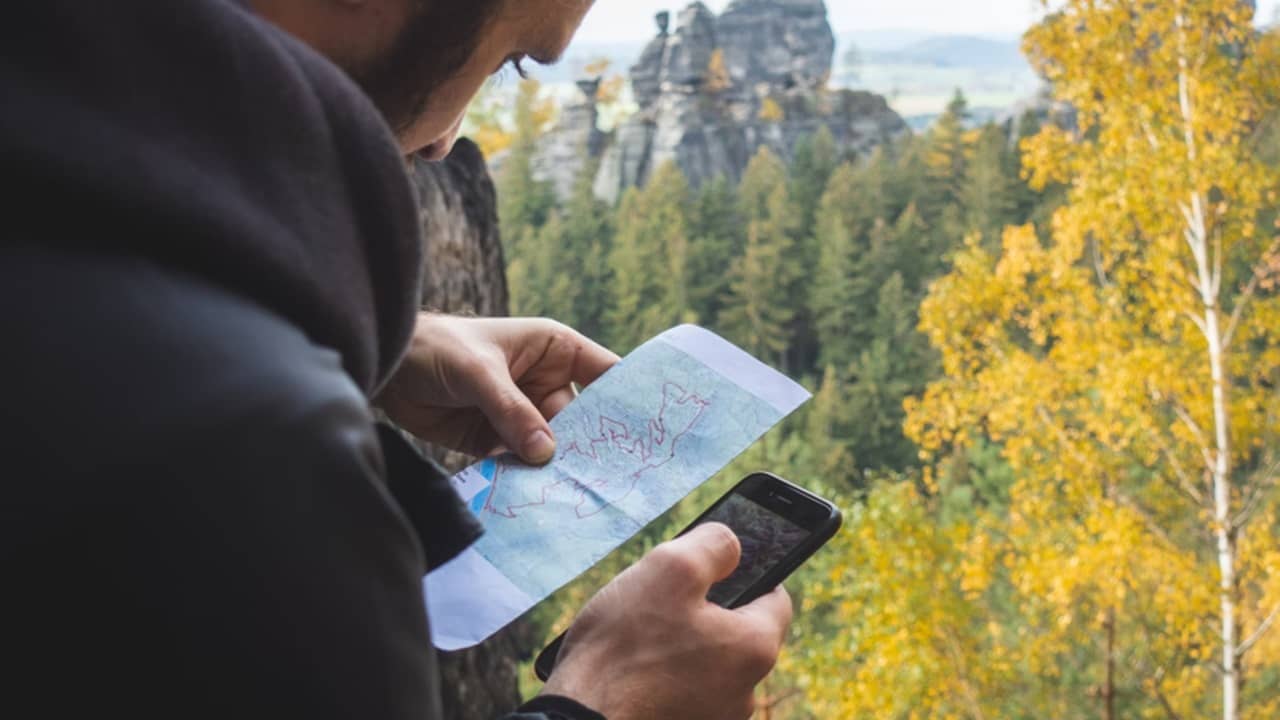 Man consulting a paper map and his phone while hiking.