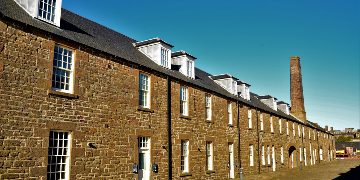 Row of brick buildings with chimneys in the background.