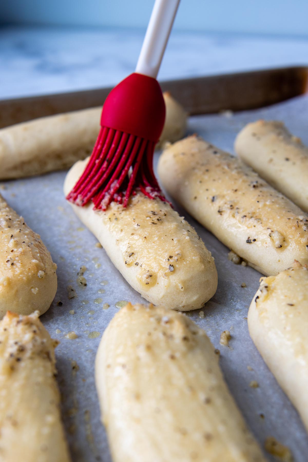 a brush putting on butter on the breadsticks