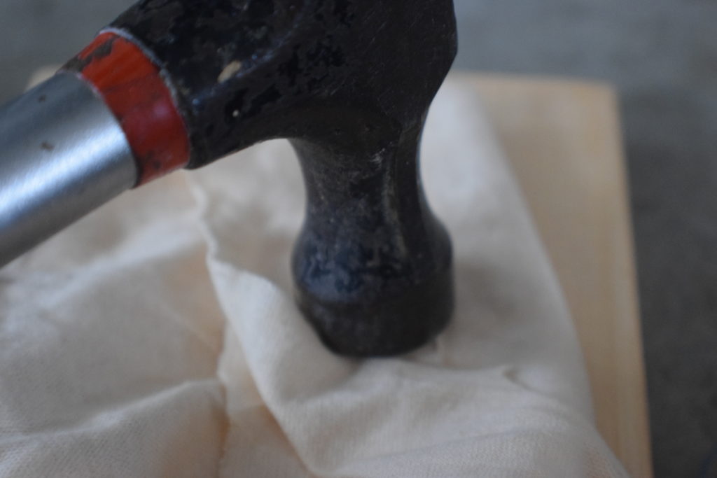 hammer hitting a rag on wood with nails inside