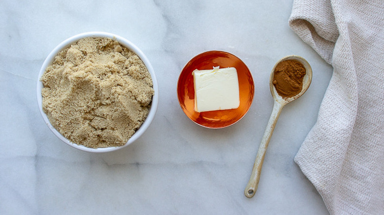 a bowl of brown sugar, a bowl of butter, and spoon of cinnamon