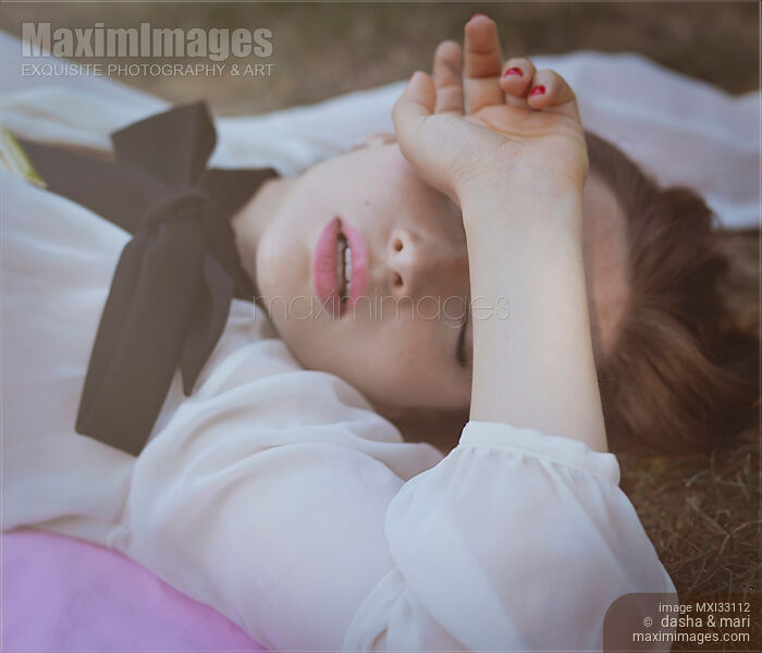 Gentle dreamy portrait of beautiful woman in classic white sheer blouse lying on the ground covering her eyes Stock Image MXI33112 © Dasha & Mari / MaximImages