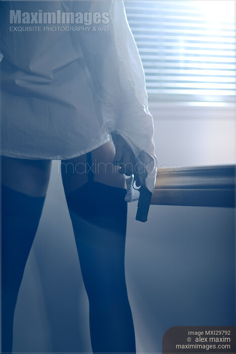 Sexy woman standing by the window with a gun in her hand wearing shirt and stockings Stock Image MXI29792 © Alex Maxim / MaximImages