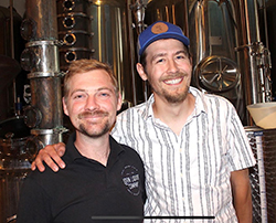 Two men in front of distillery equipment