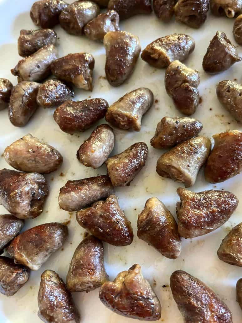 Golden-brown pan-fried chicken hearts spread across a white plate, showcasing their crispy exterior and tender texture