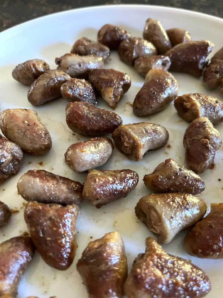 Close-up of crispy, pan-fried chicken hearts on a white plate, showing their golden-brown exterior and tender interior.