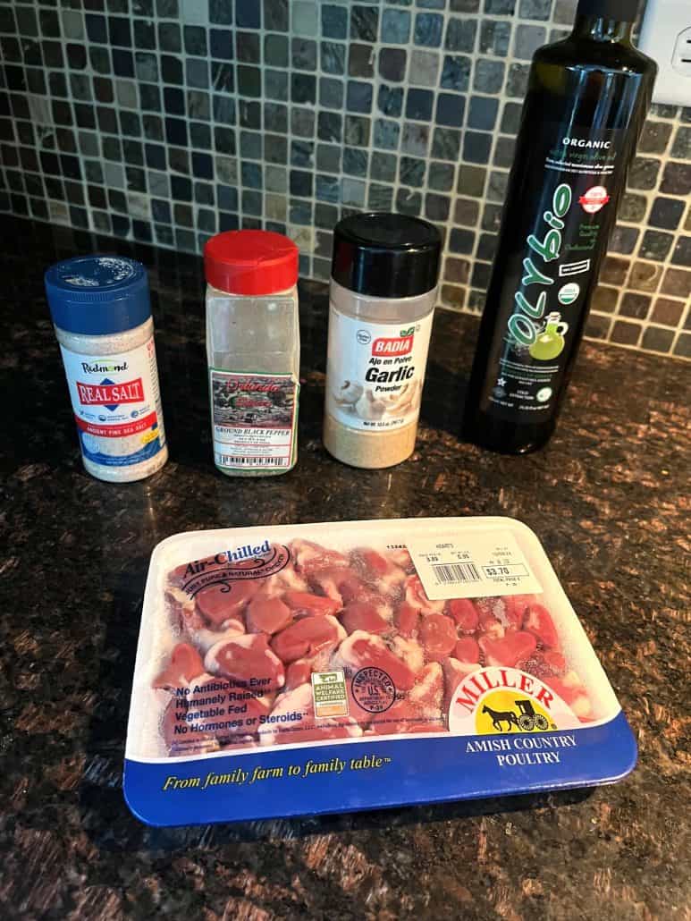 Ingredients for pan-fried chicken hearts recipe, including packaged chicken hearts, olive oil, garlic powder, black pepper, and sea salt. 