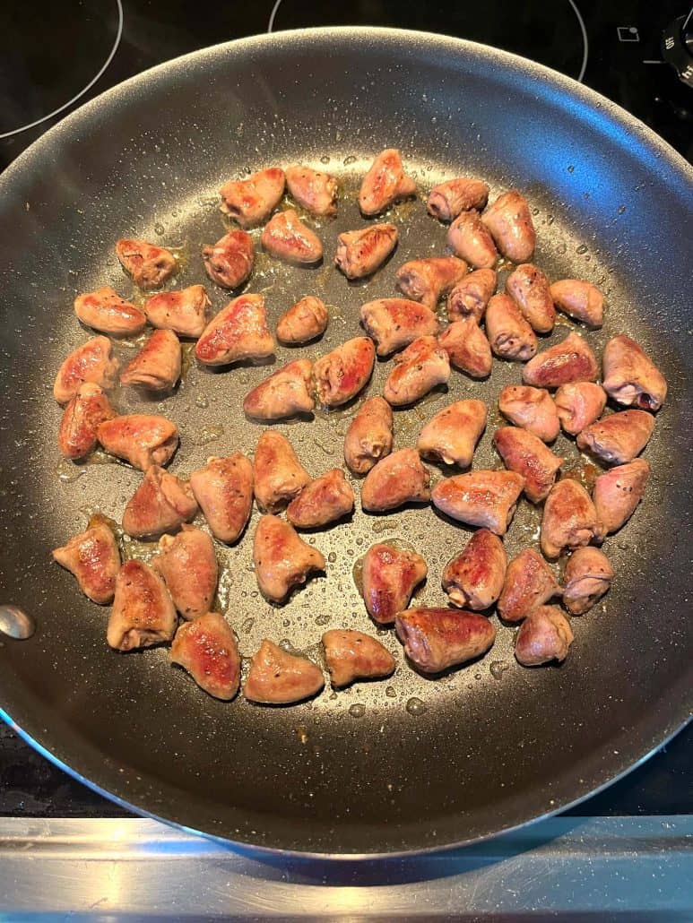 Chicken hearts sizzling in a non-stick frying pan, starting to brown evenly during the cooking process for a quick and healthy meal.