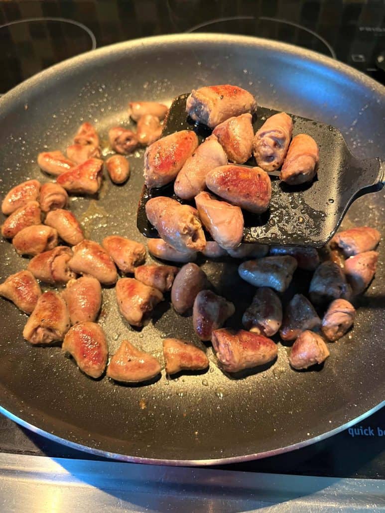 Pan-fried chicken hearts cooking in a non-stick frying pan, perfectly browned and tender.