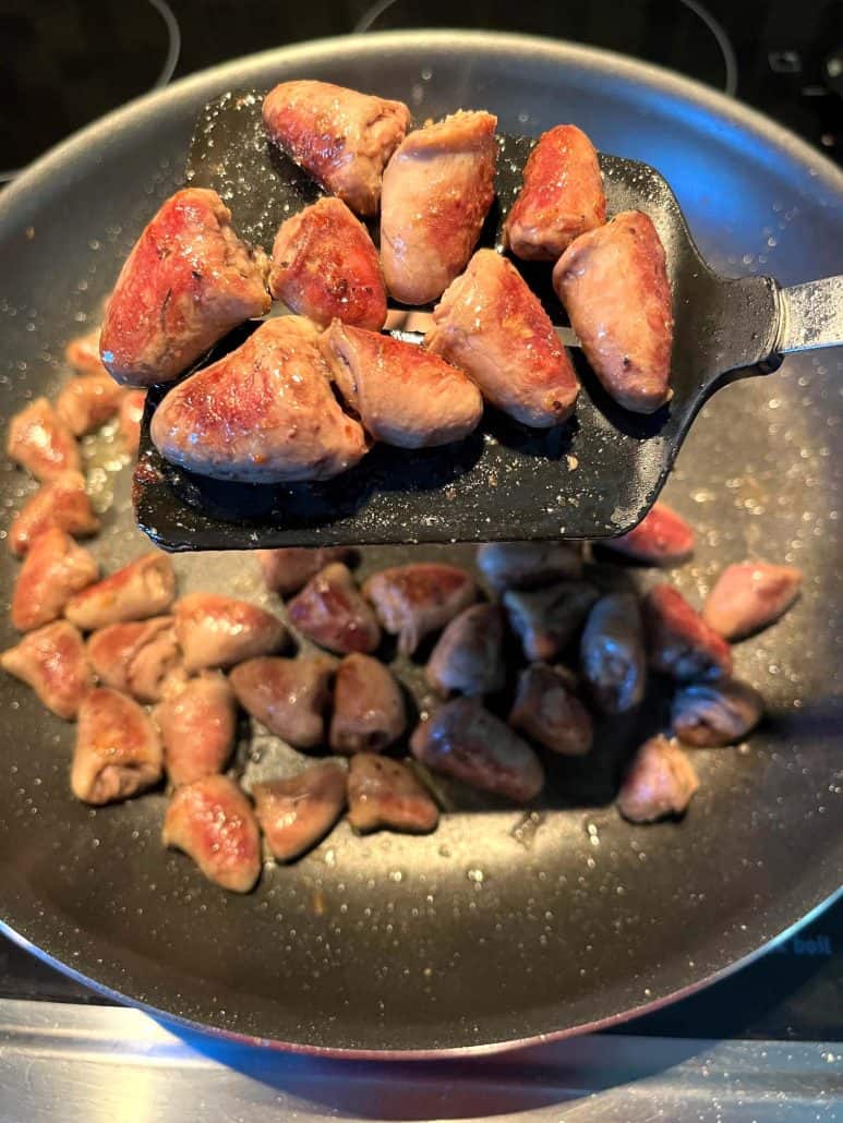 Golden-browned chicken hearts lifted on a spatula from a frying pan, showing their crispy exterior after being sautéed to perfection.