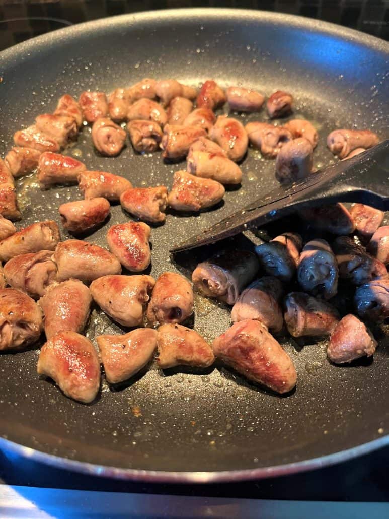 Chicken hearts sizzling in a non-stick frying pan, with a spatula stirring them to ensure even browning and cooking.