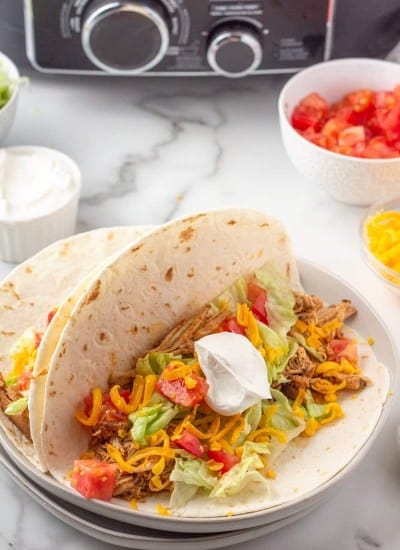 Open chicken taco in soft taco shell with lettuce, tomato, cheese and sour cream