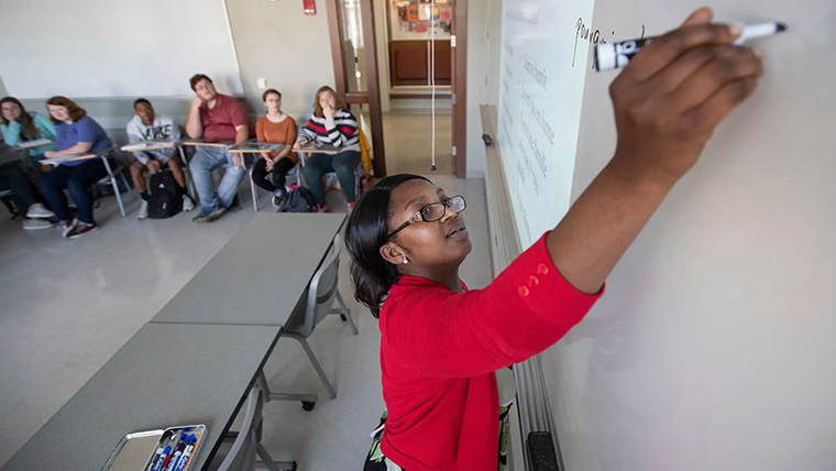 Professor writing on whiteboard in front of class