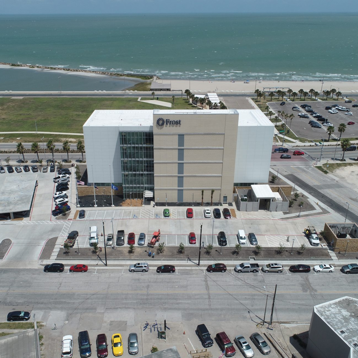 Drone view of finished Frost Bank in Corpus Christi, Texas. Parking lot with cars and ocean in the background.