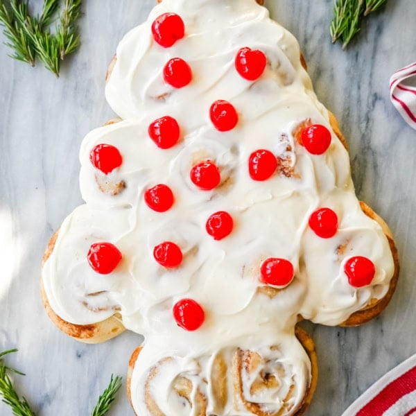 Are you looking for a sweet, festive, and delicious Christmas breakfast recipe for your Christmas morning? This Cinnamon Roll Christmas Tree is made with either homemade cinnamon roll dough or store-bought options like Rhodes frozen cinnamon rolls and covered in a creamy frosting. It can even be decorated with "red ornaments" -- maraschino cherries.