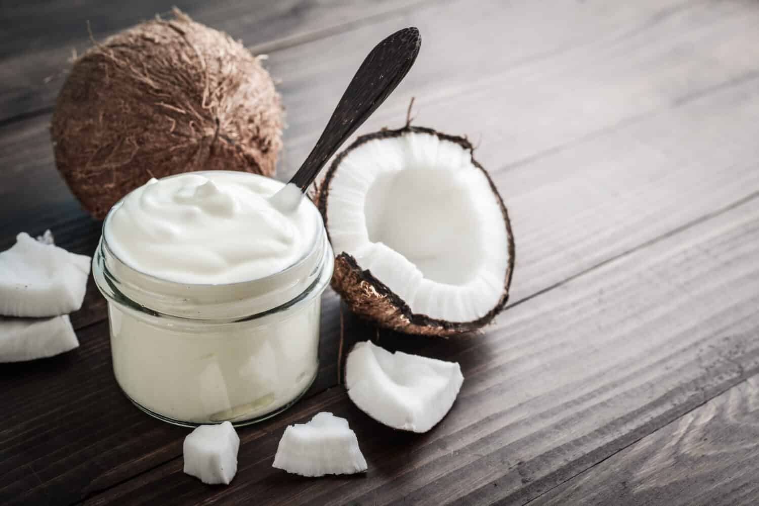 Coconut cream in a glass jar with fresh coconut on a wooden background. Healthy vegan food concept.