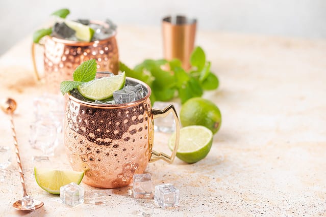 Cold Moscow Mules cocktail with ginger beer, vodka, lime. White stone background.