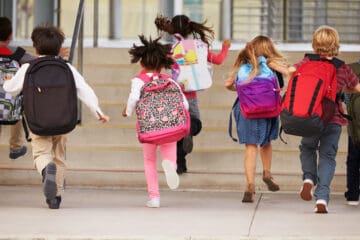 Elementary school kids running into school, back view