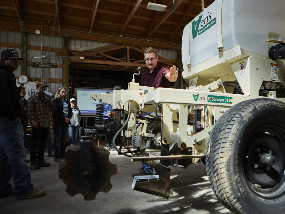 A man leans over a large soil scanner inside a tractor shop during an agriculture lesson. | MSU Photo by Adrian Sanchez-Gonzalez