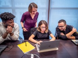 Students standing and sitting around a laptop.