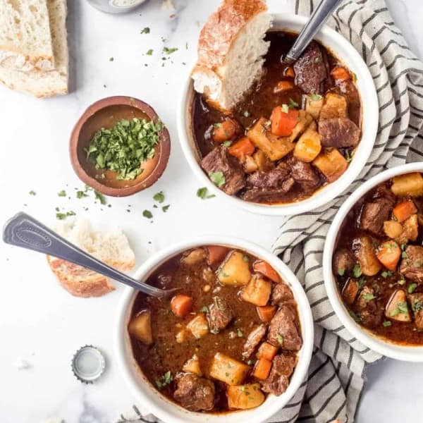 Three white bowls of Guinness stew on a white surface