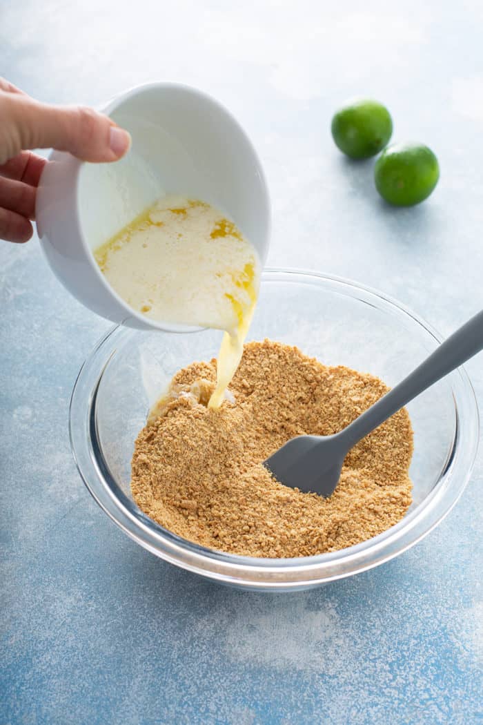 Spatula stirring together graham cracker crust crumble for key lime cheesecakes