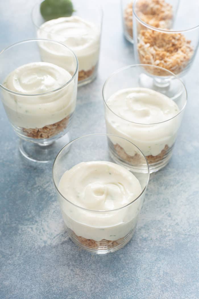 Key lime cheesecake filling on top of coconut crumble crust in individual glass dishes