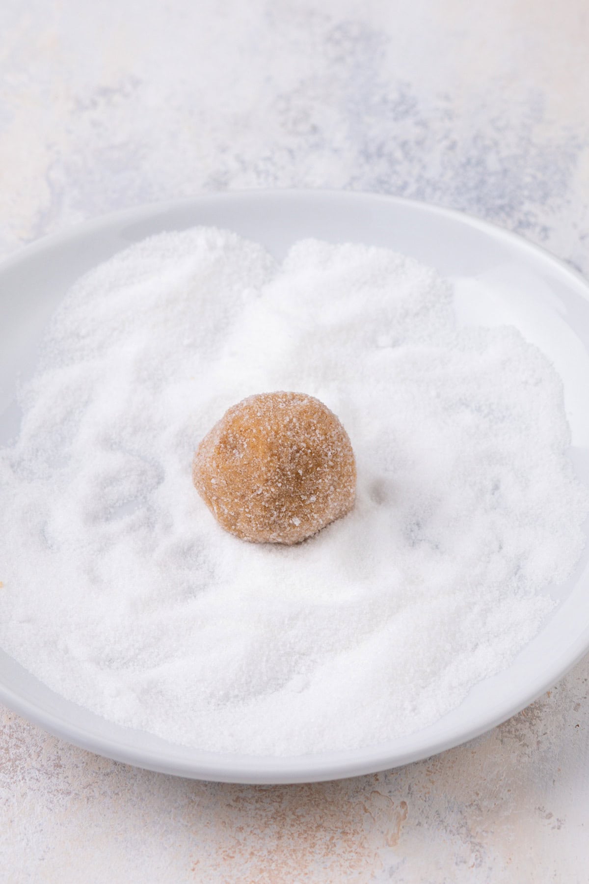 Gingersnap cookie dough ball being rolled in granulated sugar.