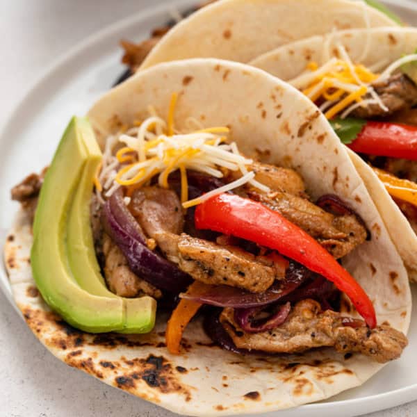 Close up of a sheet pan chicken fajita topped with cheese and avocado.