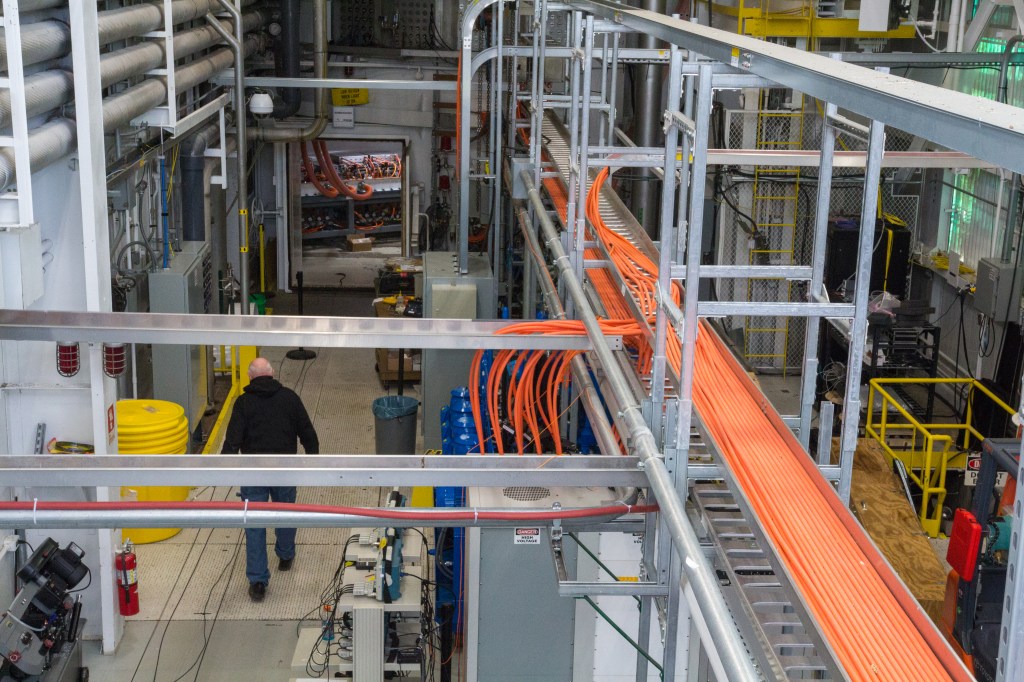 A man walks inside a large test room surrounded by hardware, cables, and metal equipment for ground testing.