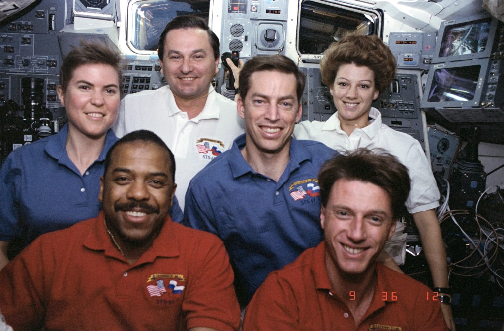 A group photo of six astronauts, four men and two women, taken on the shuttle's flight deck.