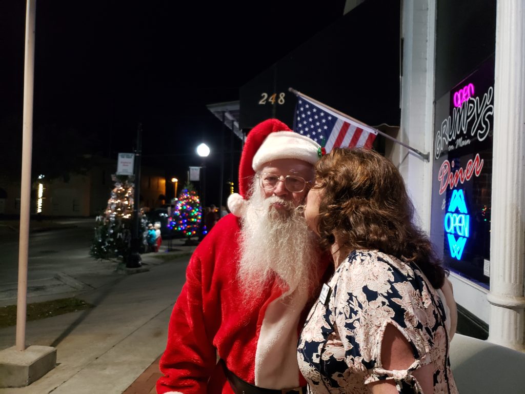 Lady whispering to & kissing Santa on the cheek