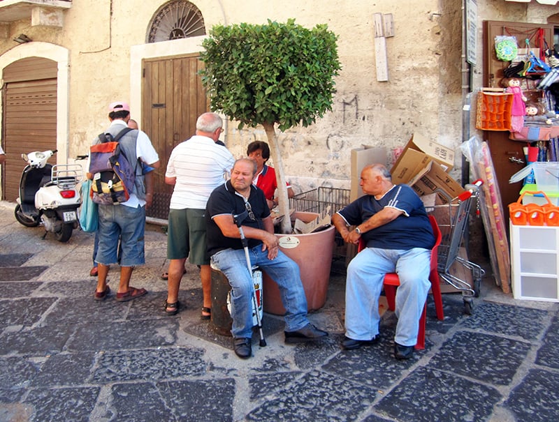 men sitting in chairs on a street in an Italian town 