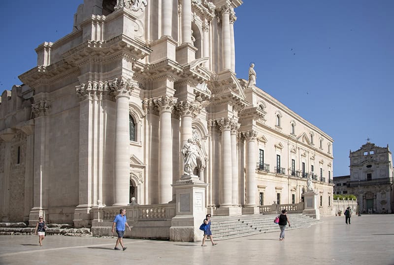 people walking by an old basilica while seeing Sicily by car