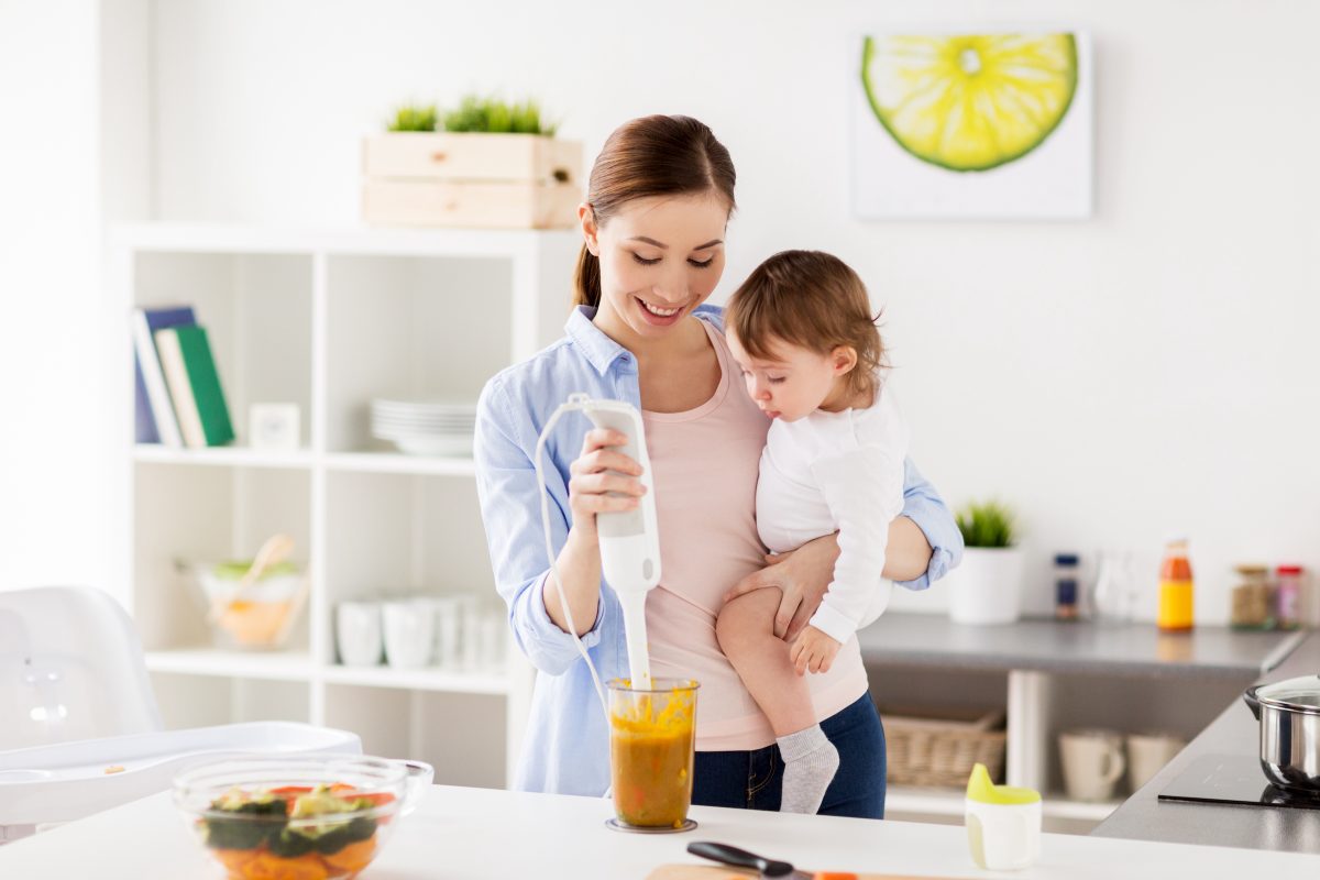 A mother holding her baby while making baby food.