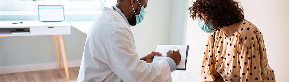 Woman consulting with her healthcare provider, who is showing her something he has written down in his exam notes.