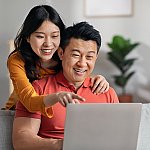 A smiling Asian couple looking at a laptop together