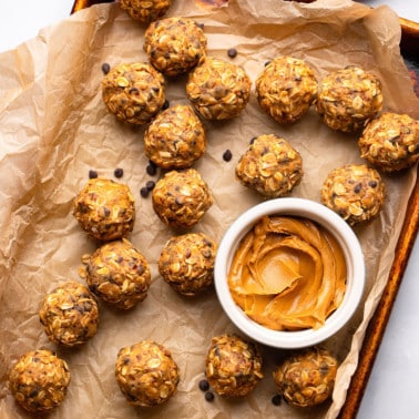 close up on peanut butter energy balls next to a small bowl of peanut butter on a parchment lined baking sheet.