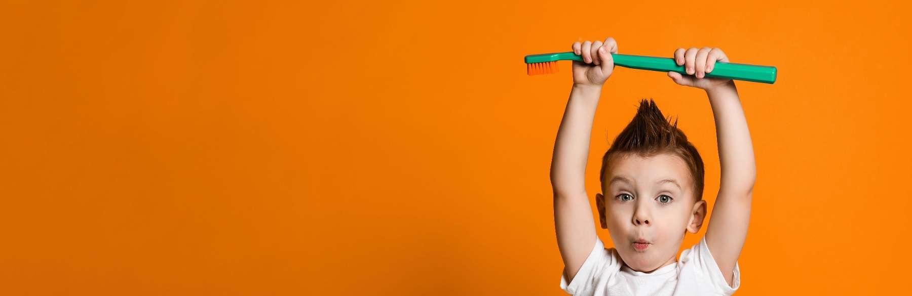 Child holding up large tooth brush at dentist near me Greeley